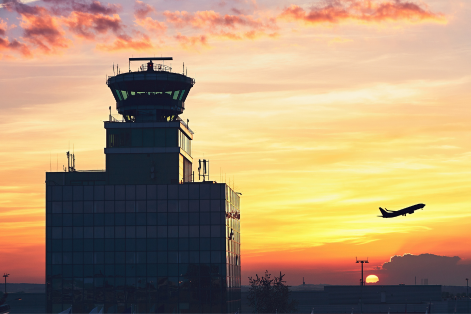 Air traffic control tower with commercial aircraft departing into sunset